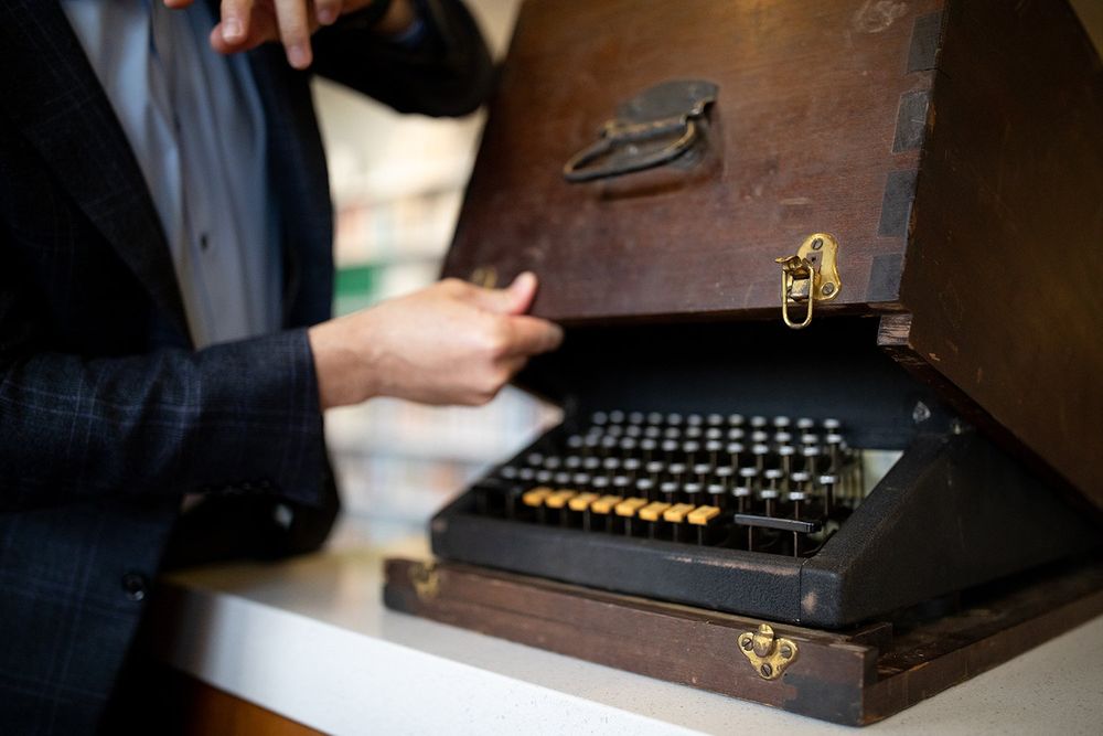 A person's hands lifting an old wooden box up to reveal a typewriter underneath.
