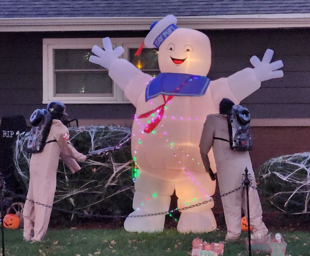 A front yard Halloween display with a tall, approximately 10 ft tall, staypuft marshmallow man with two Ghostbusters firting their proton packs at it. 