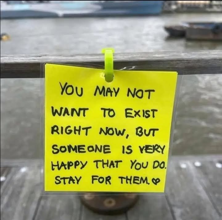 A note written on a yellow post it note that says "You may not want to exist right now, but someone is very happy you do. Stay for them." Followed with a small heart.