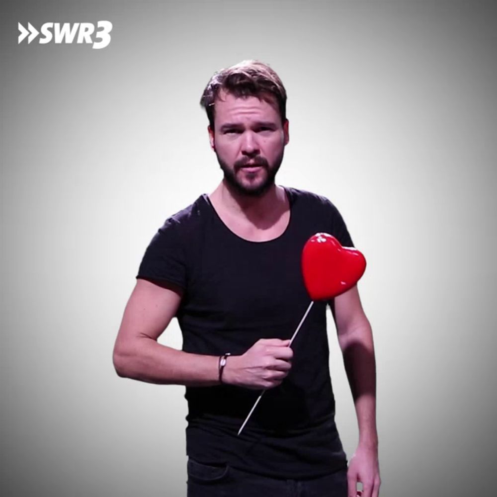 a man in a black shirt holds a red heart on a stick in front of a sign that says swr3