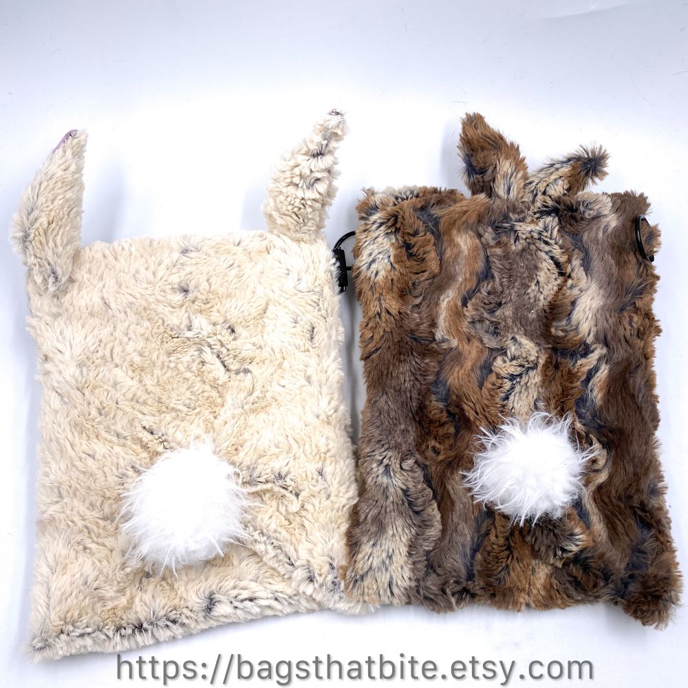 Back views of 1 white and 1 brown bunny monster crossbody bags and their white bunny tail. 