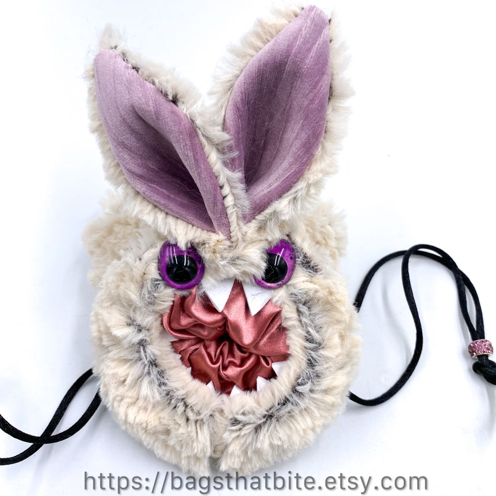 Round mouth drawstring bag with bunny ears and 2 pointy buck teeth and hand painted egg shaped eyes. Inner mouth is a shiny pink, outside faux fur is white. 