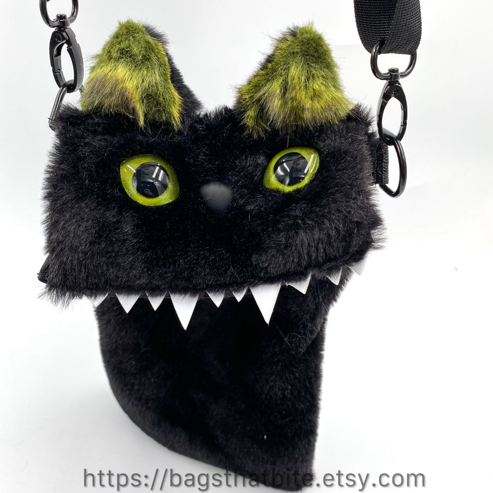 Close up of the green ear monster hanging from the adjustable removable shoulder strap. 