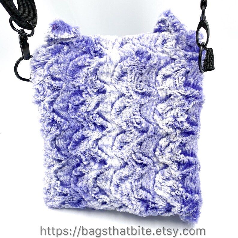 Back view of Purple and white wavy fur (that is very soft!) rectangle monster bag with cat ears, green cat eyes and soft black triangle nose. D-Rings on side allow included adjustable shoulder strap to carry bag. 