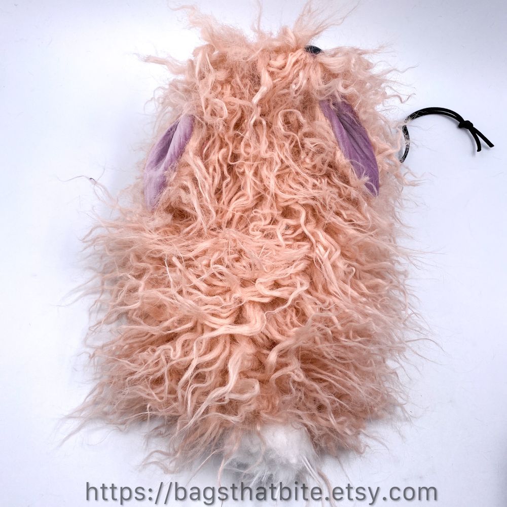 The back view of crimped pale pink faux fur round mouth drawstring bag. White cottonball tail and flop ears are featured. 