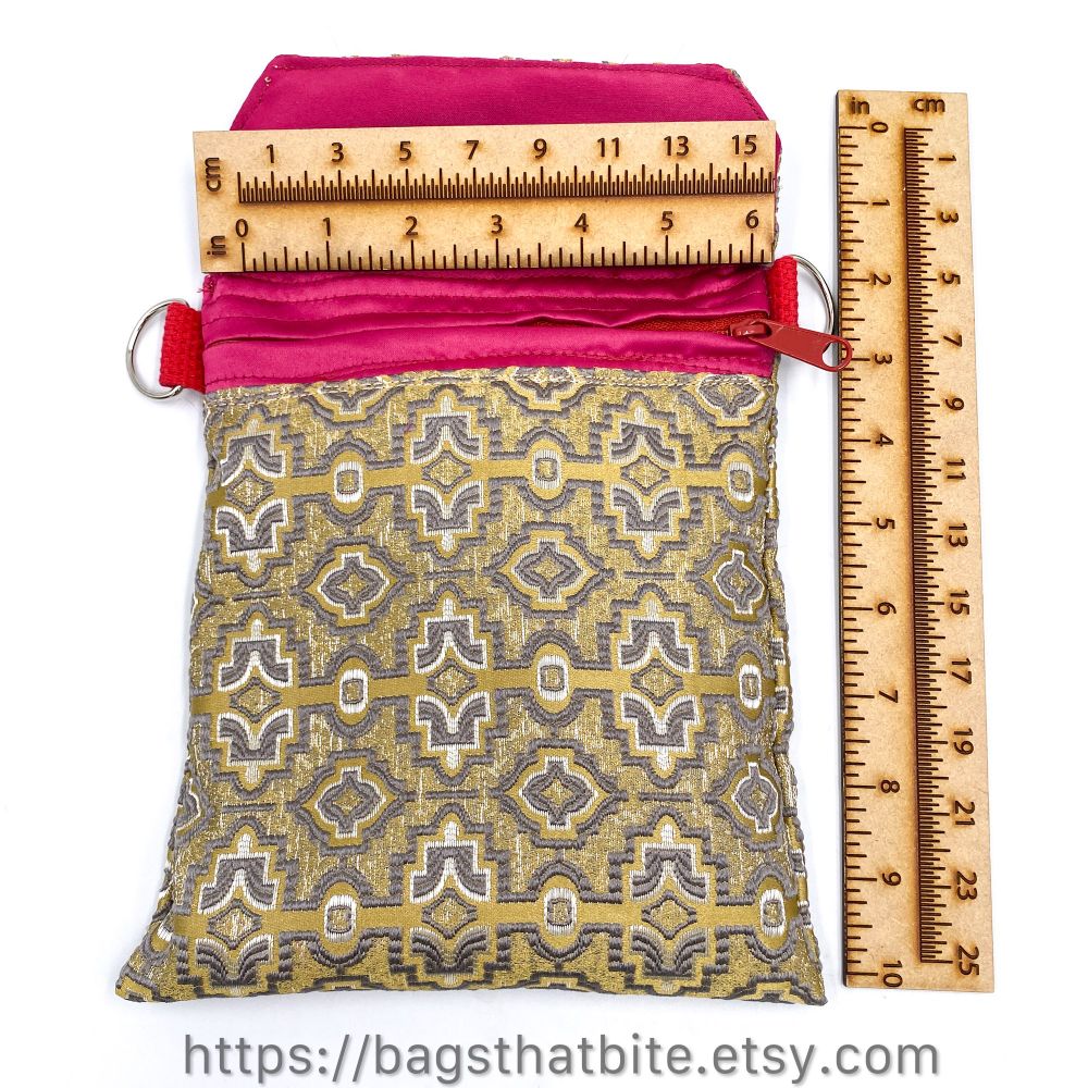 Tan rectangular monster bag with its mouth open exposing pink fabric inside with zipper, white foam teeth and two tone silver geometric embellishments embroidered on the fabric. A ruler shows the bag is 6” wide and 10” long with the zipper compartment 7” long. 