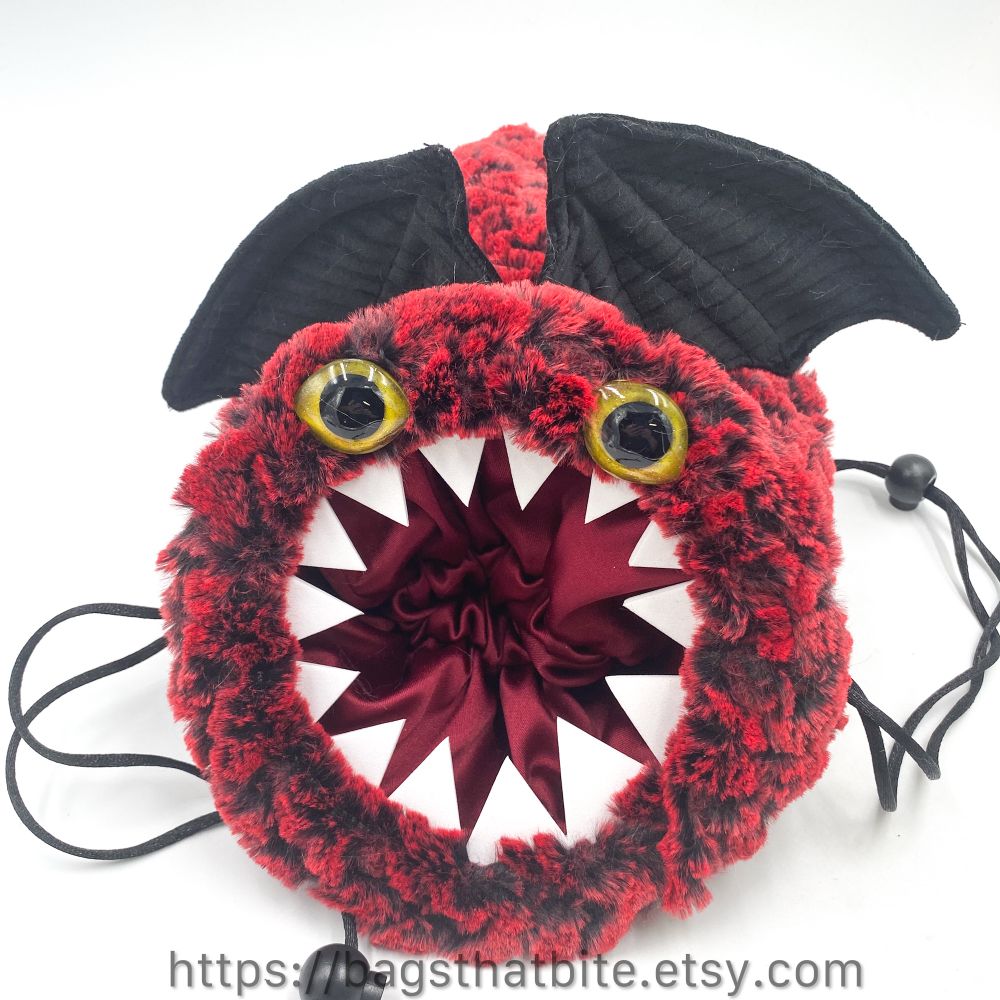 Close up of red dragonesque bag. Golden yellow hand painted eyes are on the rim of the bag staring out at you. 