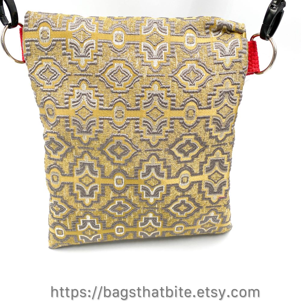 Tan rectangular monster bag with two tone silver geometric embellishments embroidered on the fabric. This is the back of the bag, silver D rings to each side with an adjustable detachable shoulder strap shown.