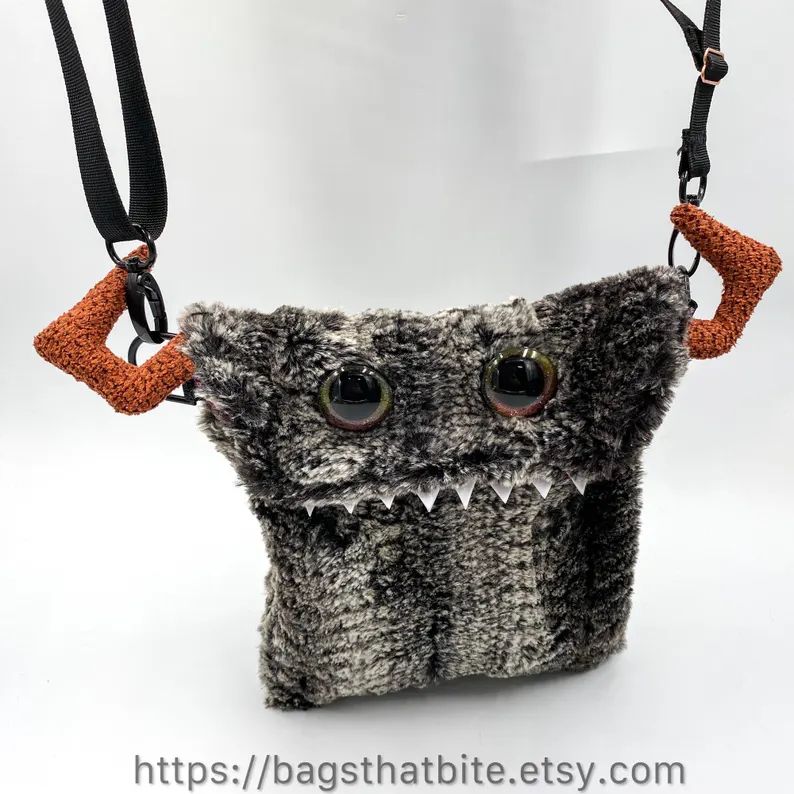 This is a crossbody (or shoulder) monster bag that is made from a faux fur of marbled gray and white with crocodile scales as a pattern. It looks fierce, but is butter soft to touch. Other than hand painted orange color changing eyes that match the orange horns popping out of the side of the bag, it has foam pointy teeth. 