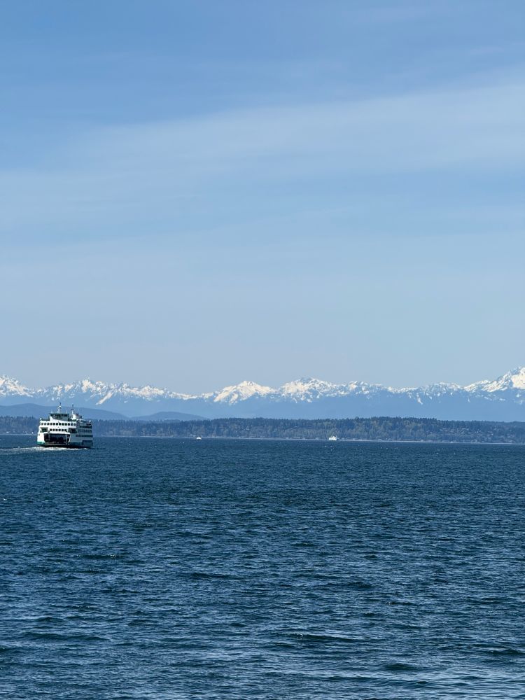 Photo of Elliot Bay with ferry in the foreground, snow-capped Olympic Mountains on the horizon and blue skies above