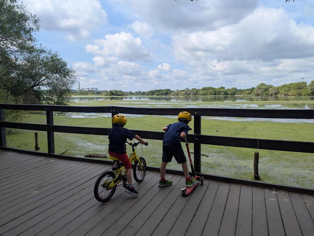 Two boys looking out at a lake with blue skies and white clouds 