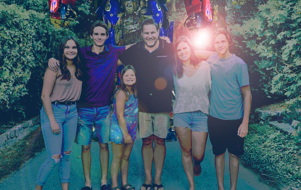 photo of a six person family, color graded with intense blacks and blue color tint with optimus prime standing in the background and an obnoxious lens flare above the families heads
