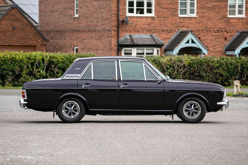 Die viertürige Stufenhecklimousine in dunklem Aubergine von der Seite: klassisches Trapezdesign mit stumpfen Winkeln und steilen Scheiben, viel Chromschmuck, kleine sportliche Rostyle-Felgen, breite C-Säule mit einem großen verchromten Entlüftungsgitter