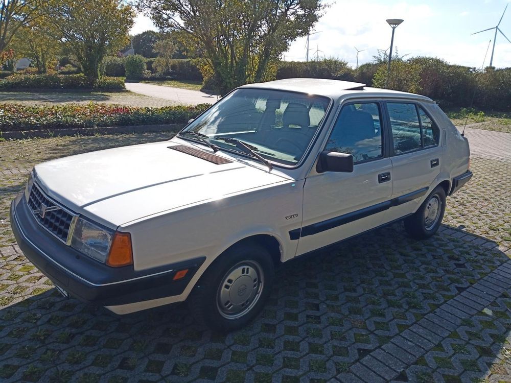 Der kompakte Volvo aus niederländischer Produktion in weiß von halb vorne: eckige Formgebung, große schwarze Stoßstange mit Chromzierstreifen, Chromgrill, rechteckige Scheinwerfer, kleine Räder mit silbernen Kappen