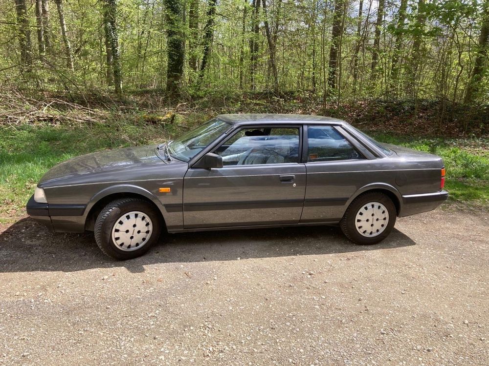 Die gestreckte, unauffällige Linie des Mittelklassecoupés in einem dunklen Silbergrau von der Seite: leichte Verjüngung nach vorne zur niedrigen Kühlermaske, breite schwarze Stoßleiste rundum, silberne Radzierblenden mit kleinen Öffnungen