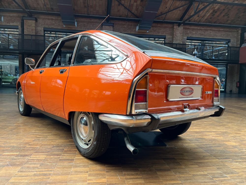 Von halb hinten: elegant gelöstes Heck mit kleiner Klappe, bei der auch der mittlere Teil der Chromstoßstange mit hochklappt, daneben oben spitz zulaufende vertikale Rückleuchten, die durch einen breiten Chromrahmen miteinander verbunden sind