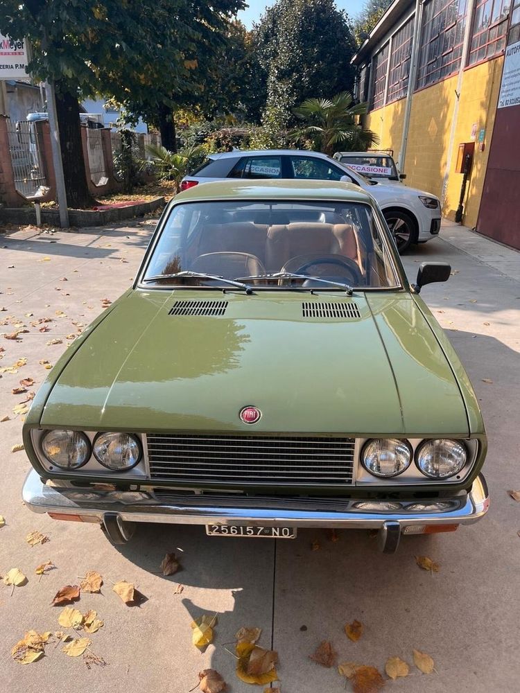 Der Fiat von vorne mit einer einfach gestyleten, aber mit viel Chrom verzierten Kühlermaske mit Doppelscheinwerfern, einer tiefen, flachen Chromstoßstange mit Hörnern und dem klassischen roten Fiat-Logo mit Kranz an der Vorderkante der Motorhaube