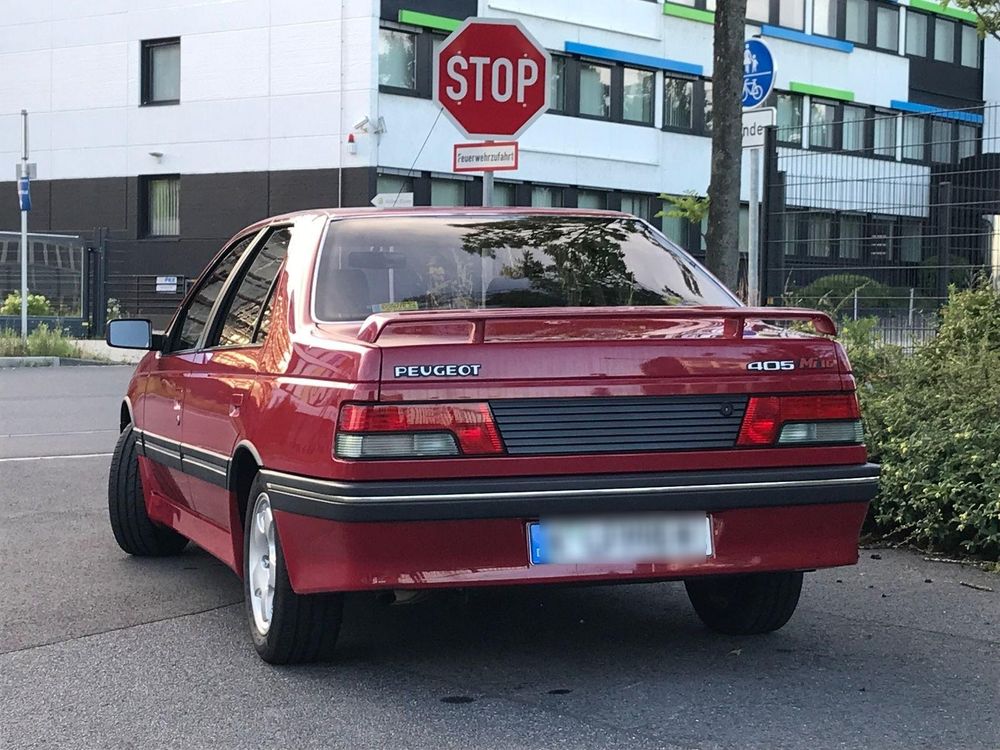 Die Stufenhecklimousine mit sportlichen Anbauteilen in Wagenfarbe von hinten: seitlich heruntergezogener Spoiler mit zwei Streben und ausgestellte Schürzen am Heck und am Schweller, die damals bei Peugeot typische umlaufende Sicke unter der Gürtellinie, die auch um die Heckblende führt, schwarze Stoßleisten mit Chromverzierung rundum, eine markante Rückleuchtengrafik und eine geriffelte schwarze Blende zwischen den Leuchten