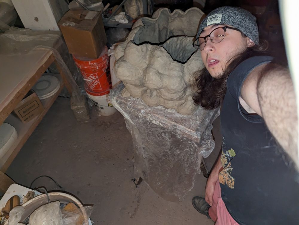 Person making faces next to a sculpture in a dirty basement.