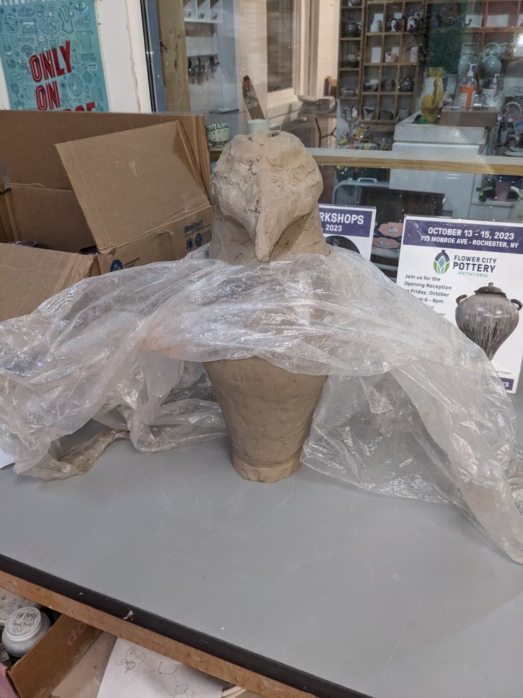 An unfinished canopic jar in front of a window with vases.