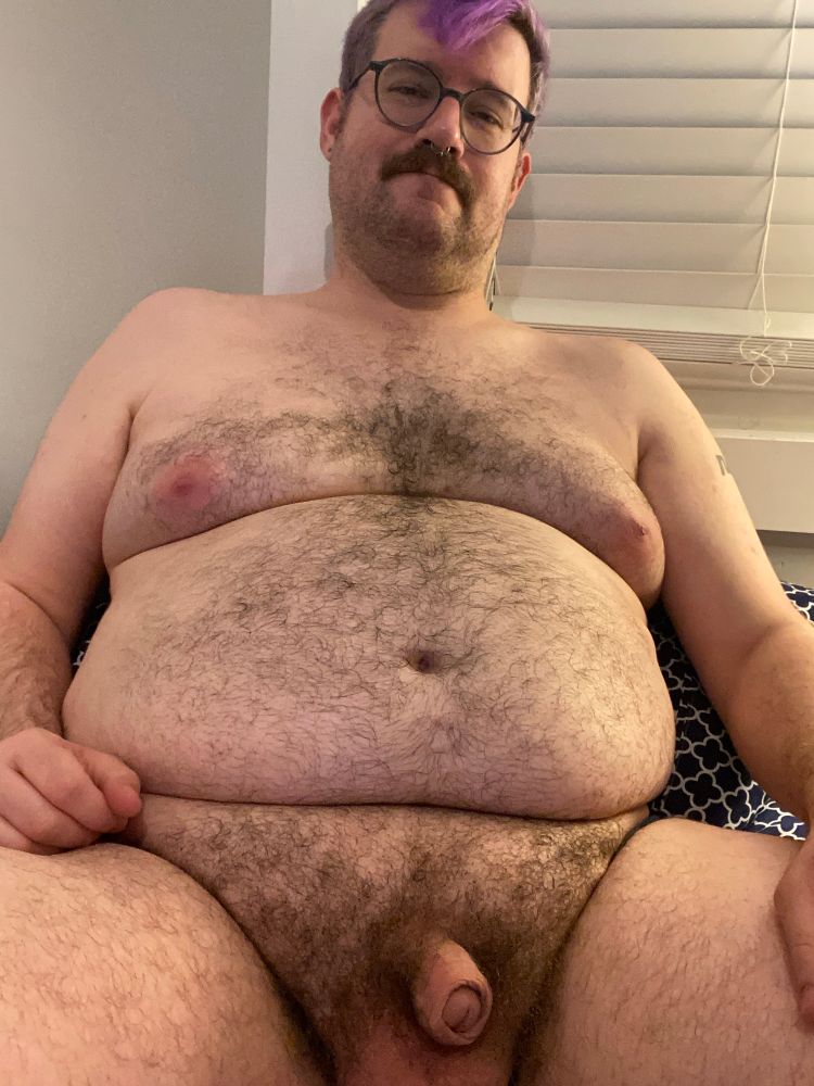 fat hairy cub sits naked in bed, small soft cock partially hooded 