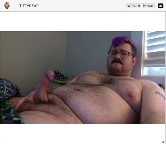 hairy bear reclining in bed as seen through a bateworld cam window, with his username and UI elements at the top of the frame. he's biting his lip and holding his stiff, curved cock at the base