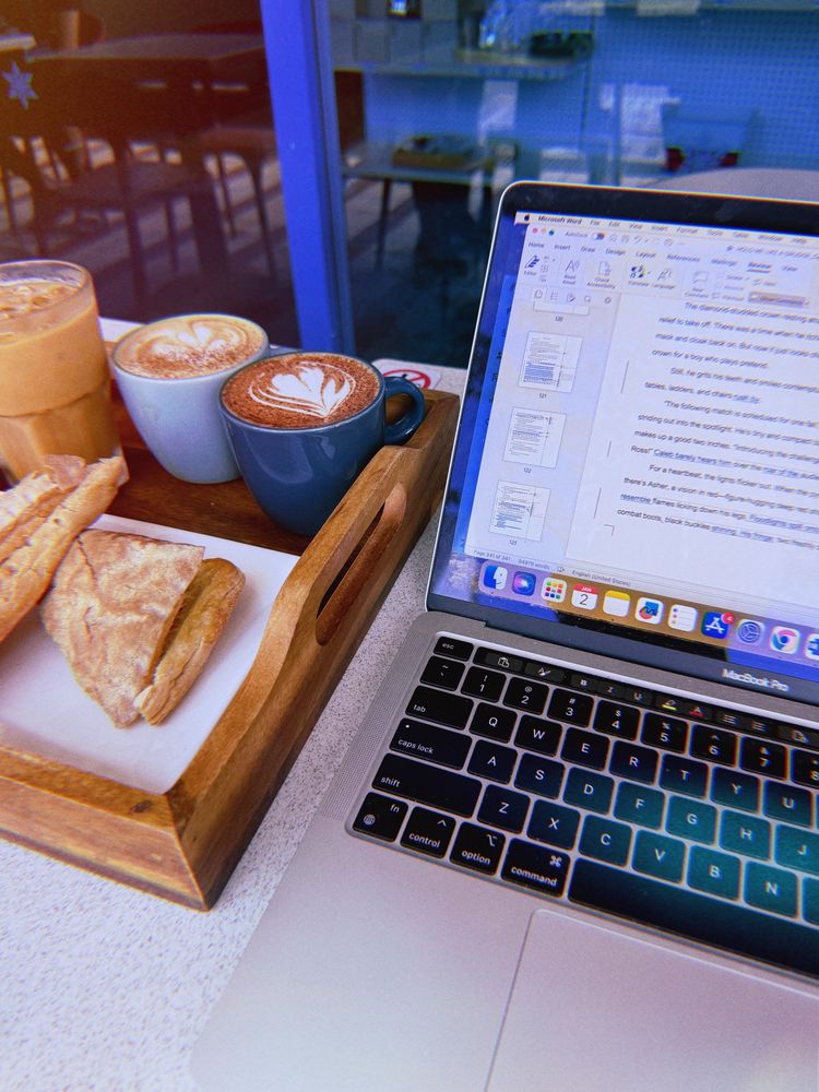 a laptop next to a tray of sandwiches and coffees at a cafe