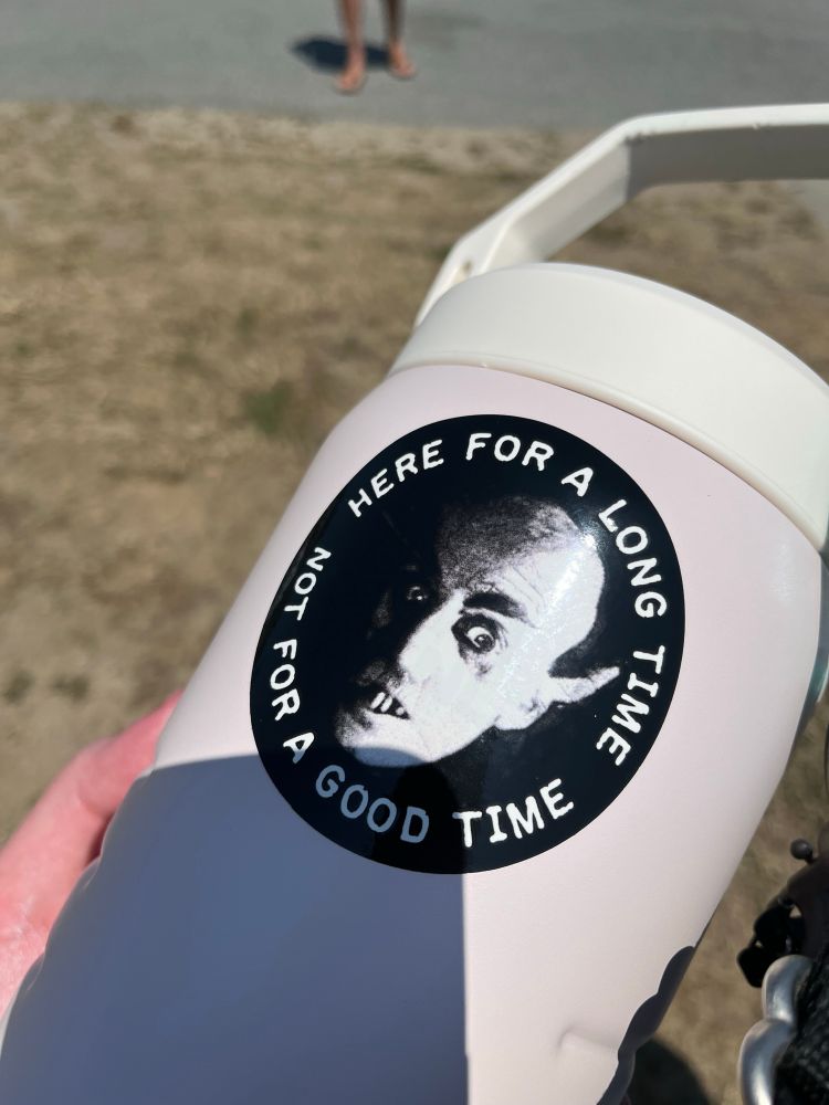 A big Stanley water bottle with a “Here For a Long Time, Not For a Good Time” sticker, with the text surrounding a photo of Count Orlok