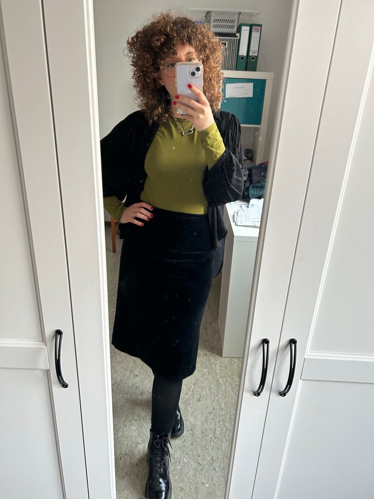 Silvia wearing black boots, black tights, a velvet midi skirt, green sweater and flowery black cardigan