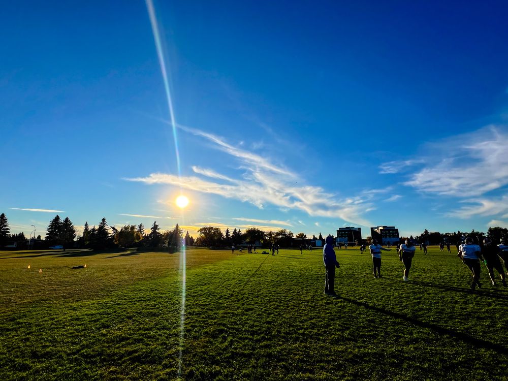 Football players during practice. Sun setting in the distance. 