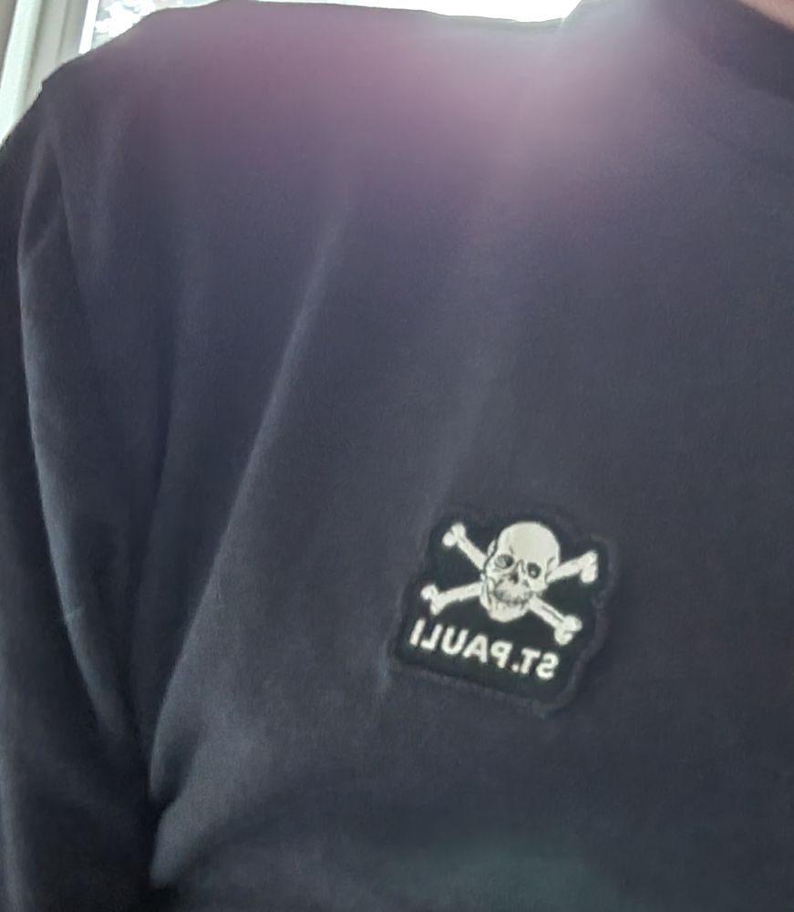 Ein schwarzes T Shirt mit einem kleinen St Pauli Aufnäher 