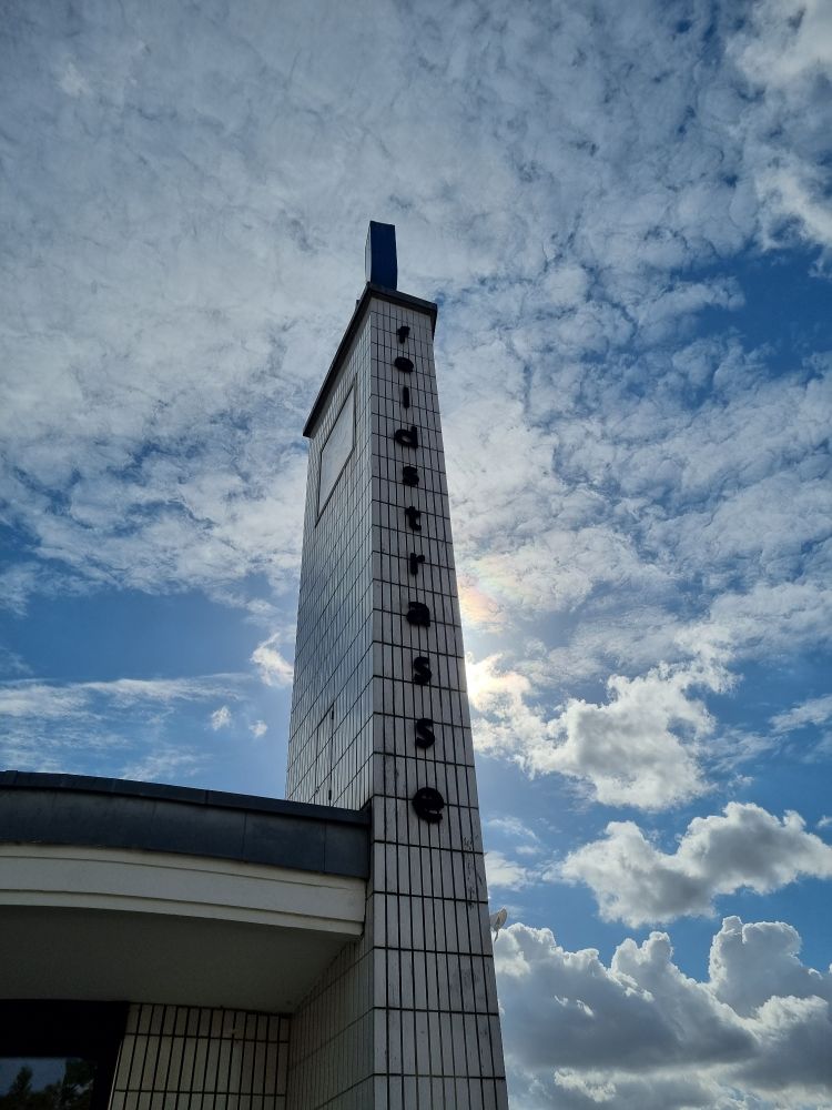 Eine schmale hohe Wand. Weiß gekachelt. Darauf steht Feldstrasse. Hintergrund, einbauen Himmel mit weißen Wolkenfetzen.
