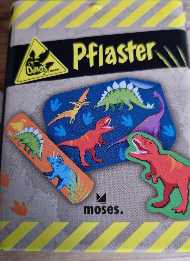 Eine Dino Pflaster Dose. Oben und unten gelbe Streifen man kann Pflaster sehen auf denen Dinosaurier sind.