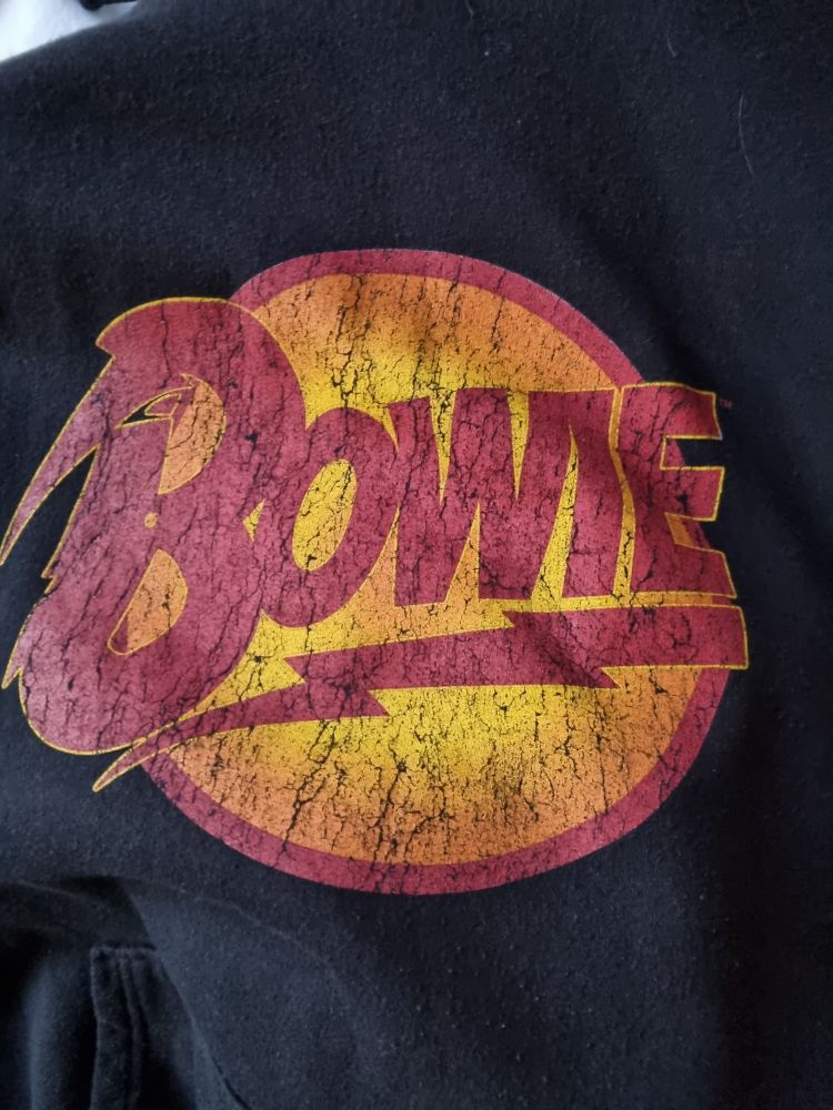 Der Name Bowie in rot vor einem gelb orangenen Kreis  ein roter Blitz unter Bowie. Das ganze auf schwarzem Hintergund.