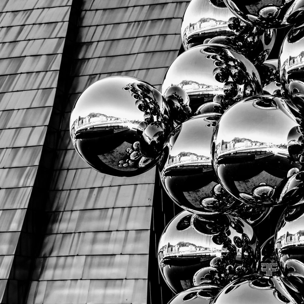 La imagen de esferas de cromo del Guggenheim evoca la fragmentación de la verdad digital. Cada burbuja refleja el mundo distorsionado por algoritmos y sesgos, simbolizando nuestras cámaras de eco en redes. Estamos conectados, pero cada uno mira su reflejo alterado, confundiendo espejismo con realidad.

Este paisaje en blanco y negro resalta la frialdad de la posverdad. Nos volvemos superficies brillantes que, aunque reflejan, no ven la verdad sólida. Es un recordatorio de cómo la hiperconexión lleva a polarización, defendiendo "nuestra verdad" sin un entendimiento común.

📍(Guggenheim de Bilbao y la escultura de Anish Kapoor)