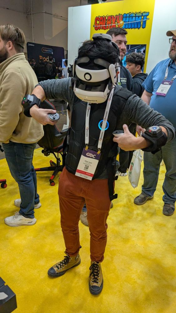 Oliver stands in the middle of a busy area of GDC and sports a bhaptics vest as he tests it in motion.