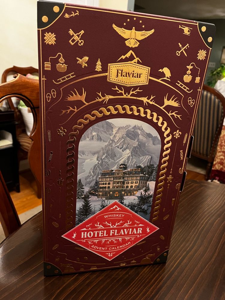 Box with Hotel imagery from. Flaviar on wood dining table with velvet upholstered furniture visible on the background   