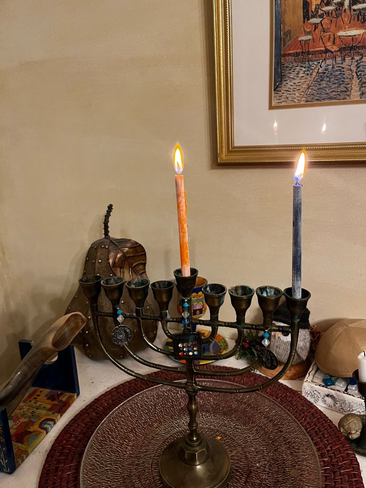 Craft style trinket channukia on a clear plate over a red woven round charger. The shamash (center candle) and 1st candle at the right hand side are lit. 