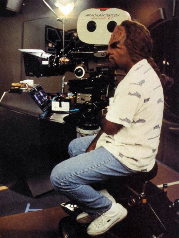 michael dorn behind the camera on the set of DS9 in worf makeup but jeans and a collared shirt