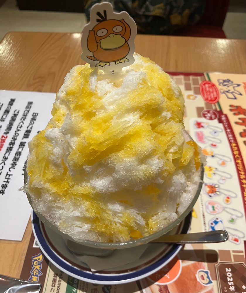 コメダ珈琲店のポケモンとのコラボのコダックのマンゴーミルク氷です。かき氷にコダックのイラストが描かれたピックが刺さってます。