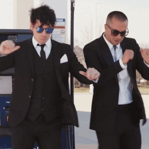 two men in suits dancing in front of a gas pump that says notice on it