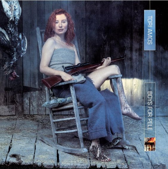 The image is the cover for Tori Amos' album "Boys for Pele". It features the singer sitting in an old rocking chair on a ramshackle porch. A snake slithers under the chair. Amos's feet and legs are covered in mud and she is dressed in rags. 