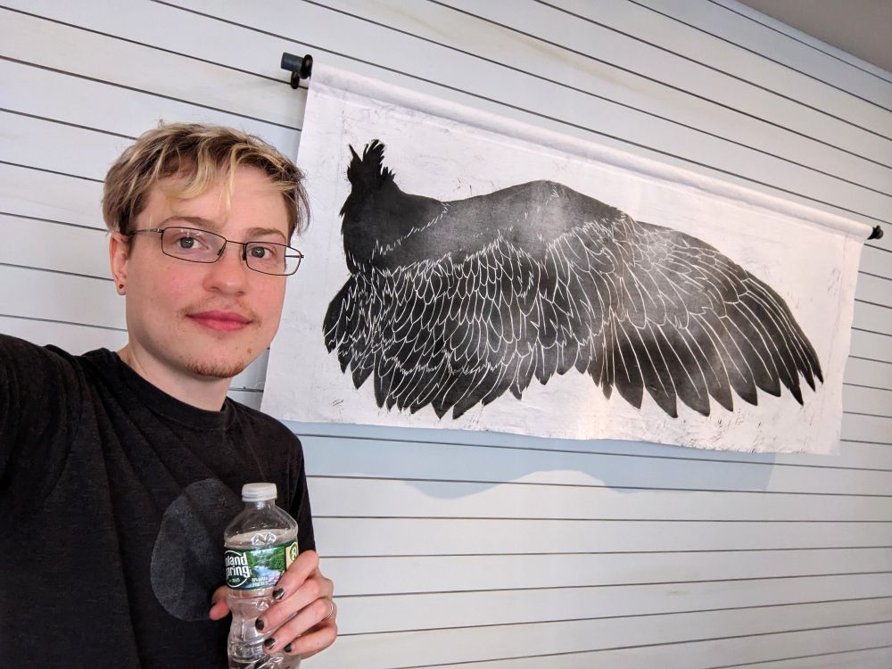 Jaime Wing posing in front of a large scale (5 foot) wood block print on fabric of a crow's wing.