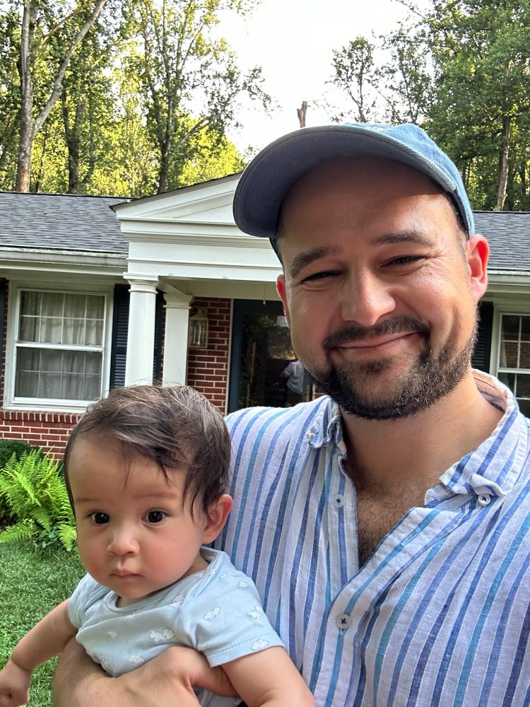 The cutest baby giving gen z stare even if her wrong gen against brick house background and a very tired uncle who is working remotely 