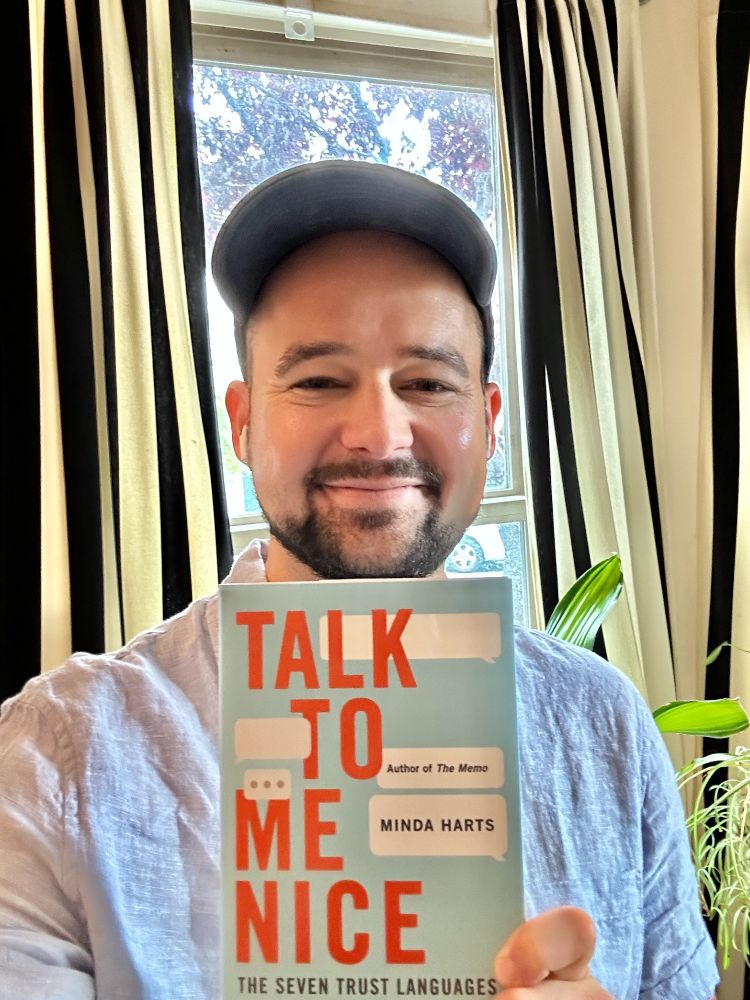 Tired Tristan holding a copy of Minda Harts new book "Talk to me nice" 
