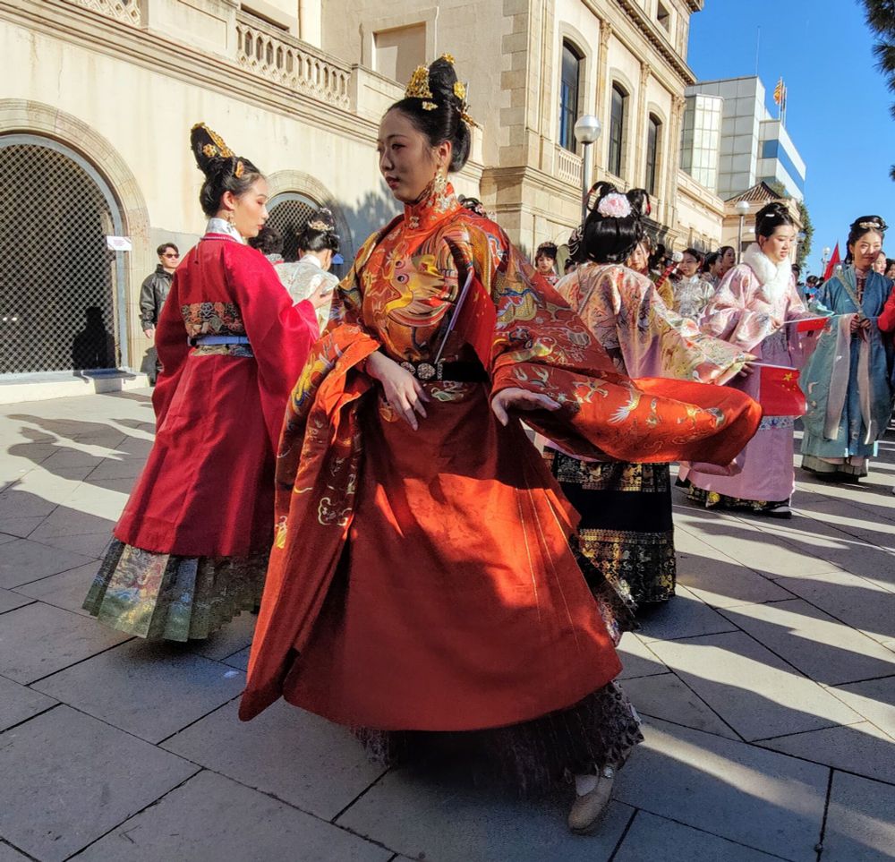 Mujer con vestimenta ceremonial china bailando en la celebración del Año Nuevo Chino. Detrás tiene a otras compañeras acompañando en la coreografía. 