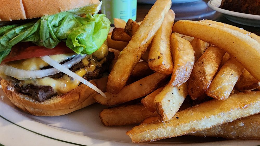 A double cheeseburger with onion, lettuce, tomato and a side of fries. 