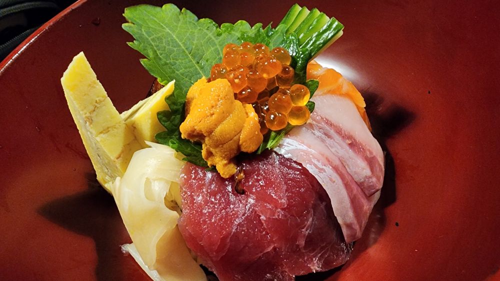 A bowl of assorted sashimi, roe, egg, and urchin. 
