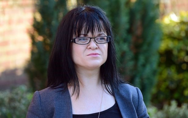 Erin Pritchard wearing a smart jacket with long dark hair flowing, and glasses.