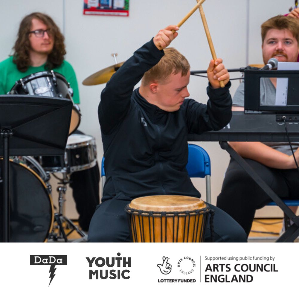 A young person enthusiastically plays a djembe drum with drumsticks, surrounded by other musicians, including a drummer and a keyboard player. The scene takes place in a bright indoor setting. Logos at the bottom indicate support from DaDa, Youth Music, the National Lottery via Arts Council England, and Arts Council England